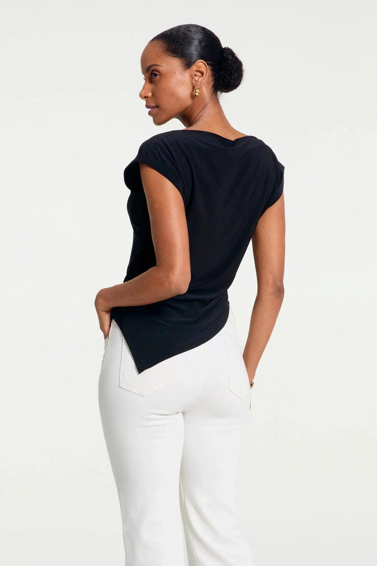 Back view of women’s asymmetrical draped top styled with white pants
