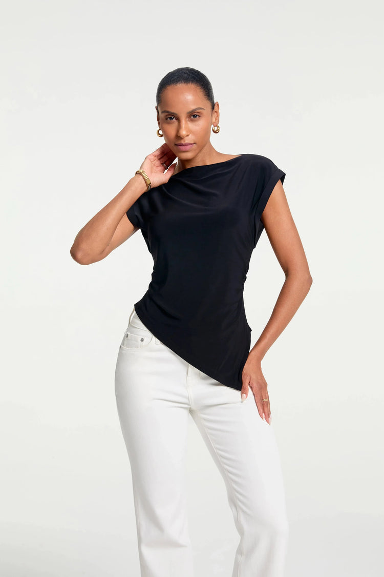 Women’s asymmetrical draped top styled with white pants, full-body front view