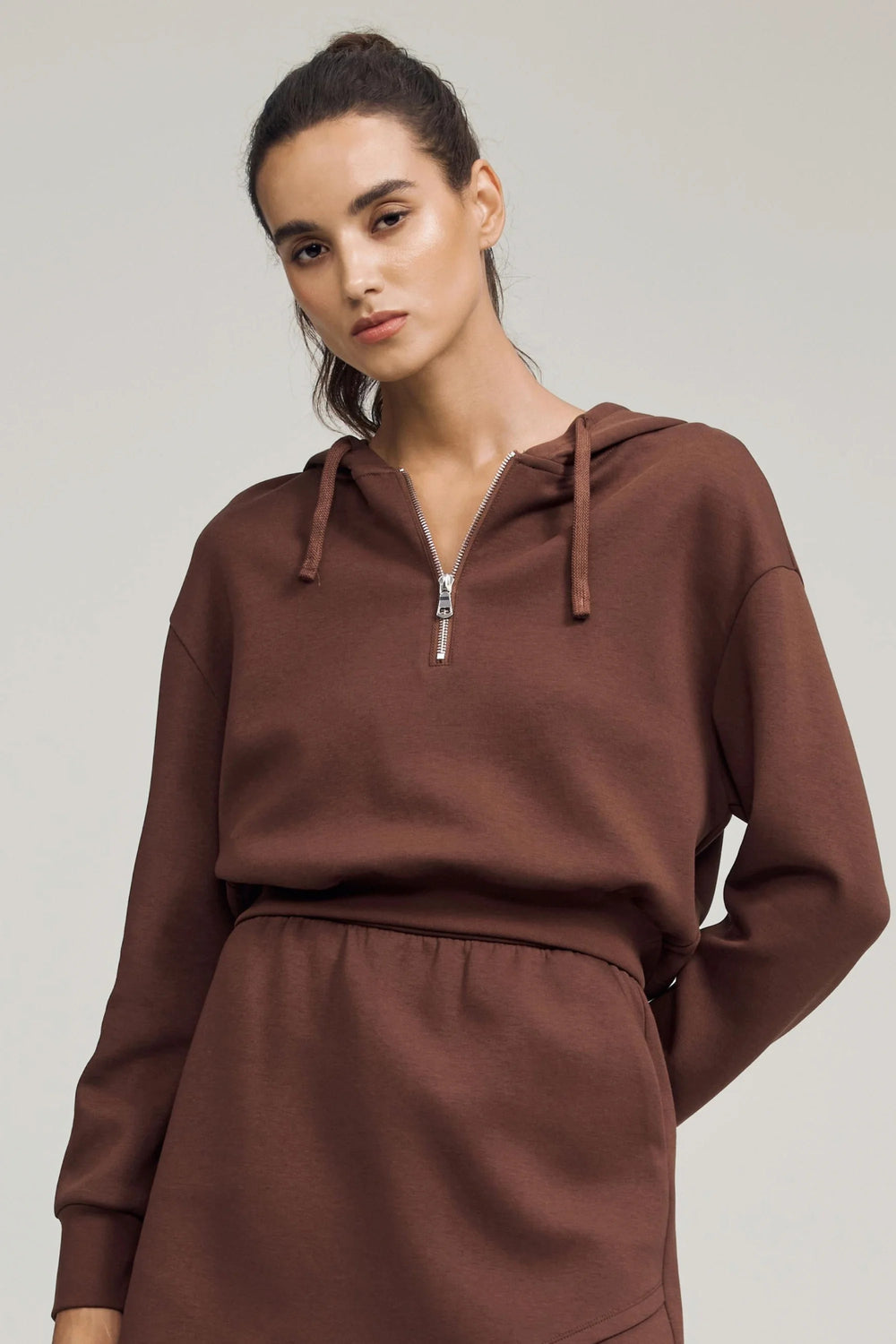Cropped half-zip fleece hoodie in chestnut brown styled with a matching skirt, front view