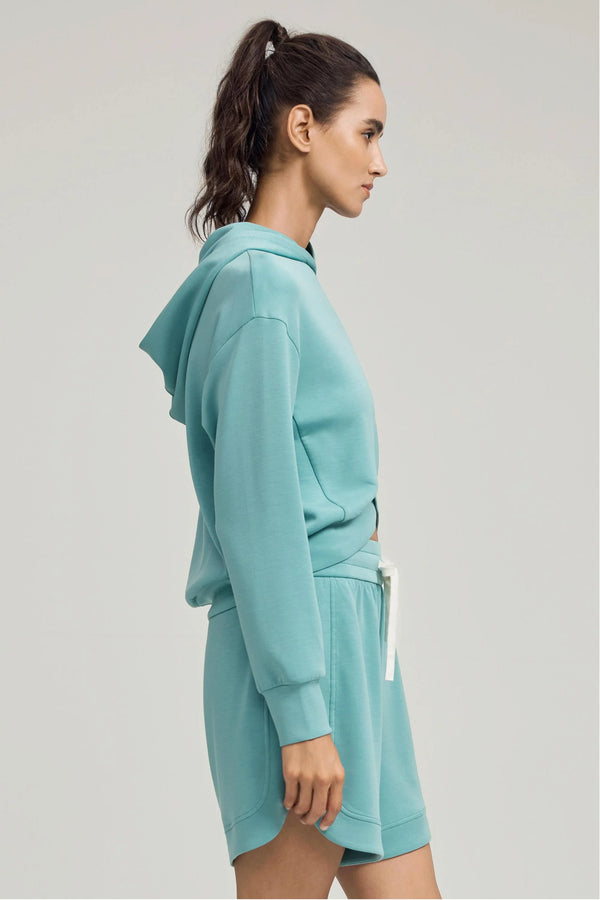 Side view of a crossover hem hoodie in seafoam blue with dropped shoulders and easy drape
