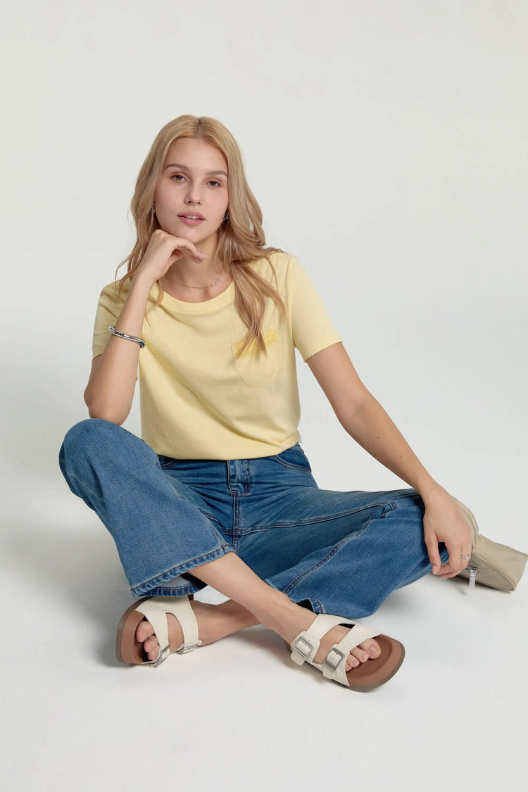 Women’s sunbeam yellow lace-trim pocket tee worn seated, styled with blue jeans