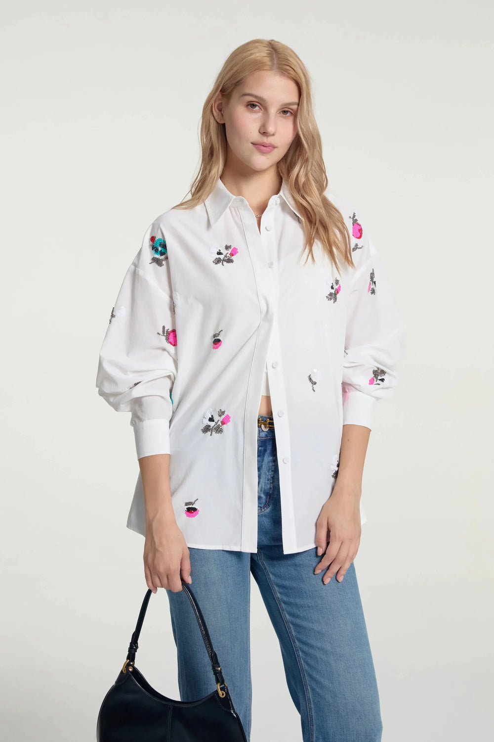 Oversized embroidered button-down shirt styled with blue jeans and a handbag, front view on grey background