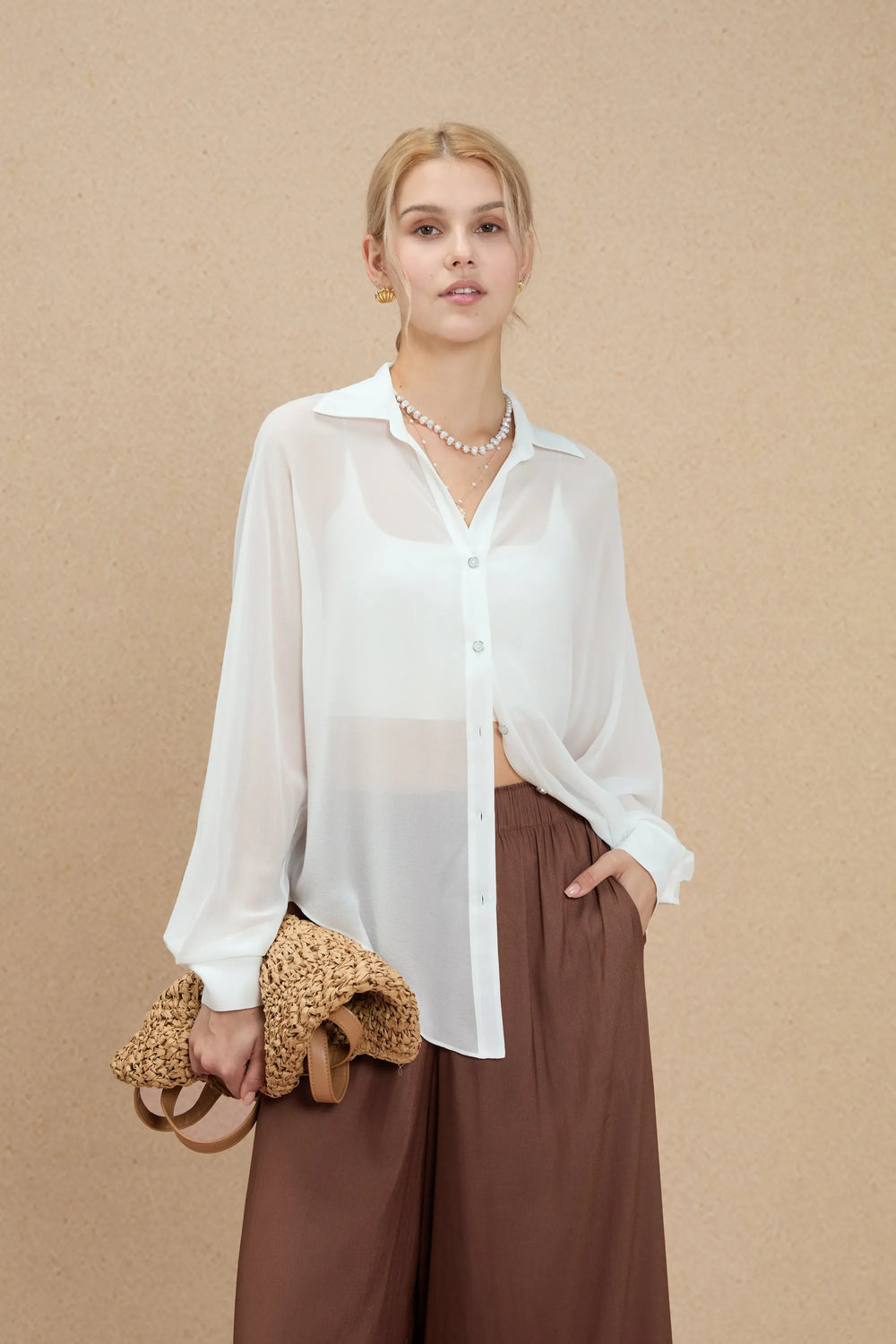 Sheer white silk oversized button-down shirt styled with brown wide-leg trousers, front view