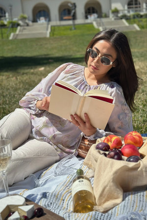 Sheer silk peasant blouse with lavender florals styled with linen trousers in a park setting