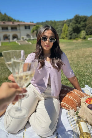 Women’s soft knit hook-front cardigan worn with sunglasses and linen pants, holding a champagne glass