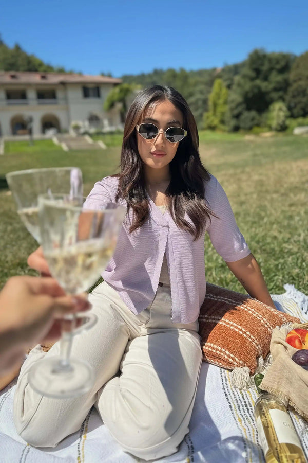 Women’s soft knit hook-front cardigan worn with sunglasses and linen pants, holding a champagne glass