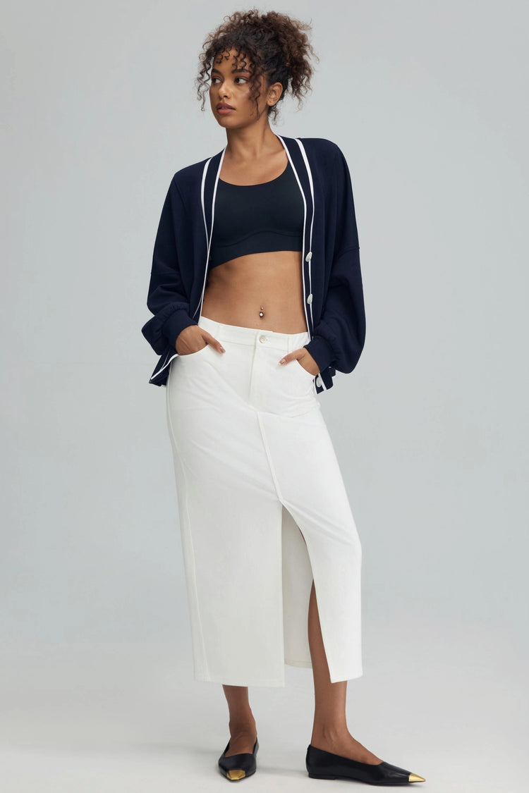 White stretch denim maxi skirt styled with a navy cardigan and black sports bra for a modern, layered everyday look.