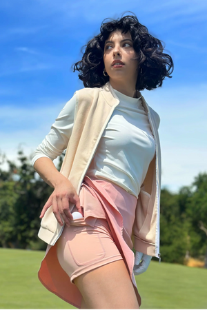 Side view of a refined zip-front vest in oatmilk beige styled with a pink athletic skirt