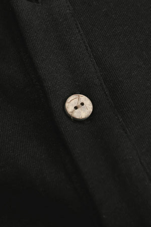 Detail view of the button closure on a men’s onyx black linen–Supima button-neck henley.