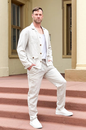 Side view of a men’s driftwood beige linen-Tencel safari jacket worn outdoors on stairs, showing a structured yet relaxed fit.