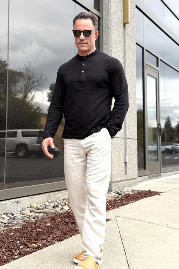Men’s onyx black linen–Supima button-neck henley worn with linen pants, shown walking outside a café.