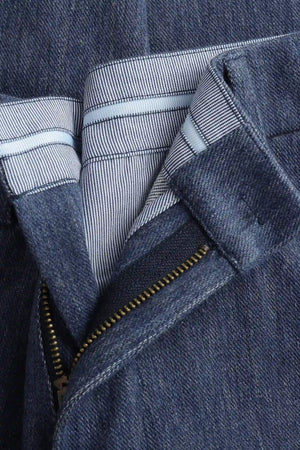 Close-up of the waistband detail on men’s indigo rinse structured denim trousers, showing tailored construction and clean finish.