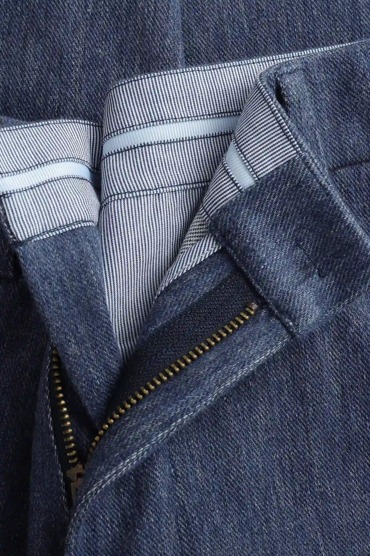 Close-up of the waistband detail on men’s indigo rinse structured denim trousers, showing tailored construction and clean finish.
