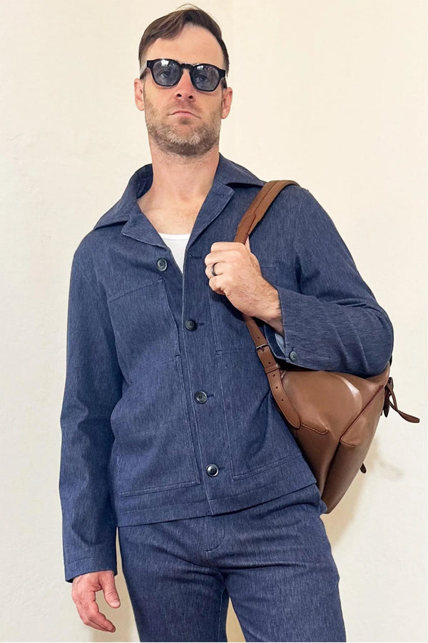 Front view of a men’s indigo rinse utility denim overshirt jacket styled with matching denim trousers and a brown crossbody bag.