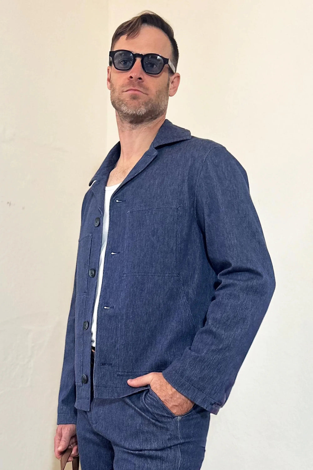 Front view of a men’s indigo rinse utility denim overshirt jacket styled with matching denim trousers and a brown crossbody bag.